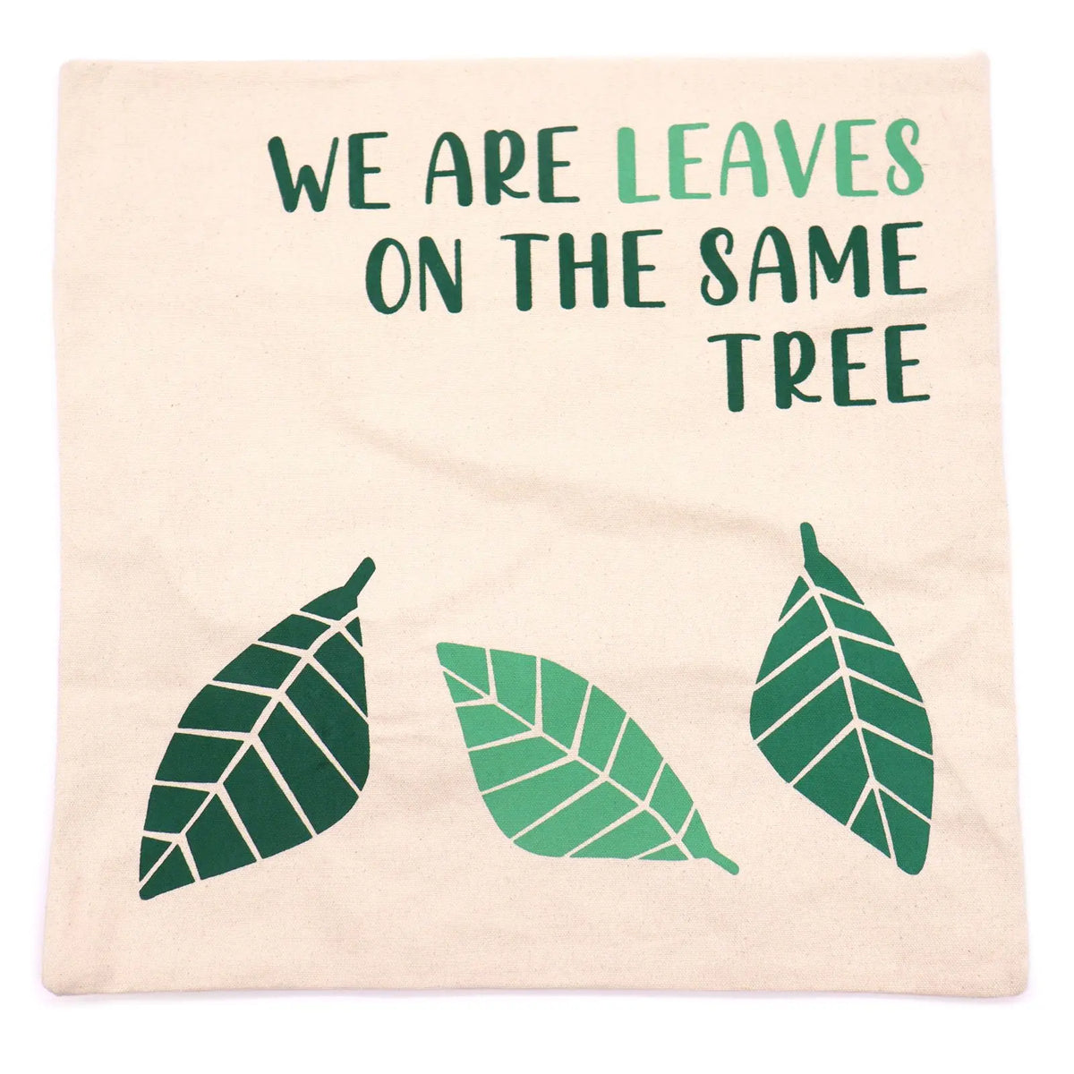 Funda de cojín de algodón natural con estampado de hojas verdes y la frase "WE ARE LEAVES ON THE SAME TREE".