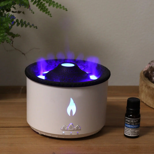 Difusor de aromas efecto volcán, blanco y negro, con luz LED azul y botones de control, junto a aceite esencial.