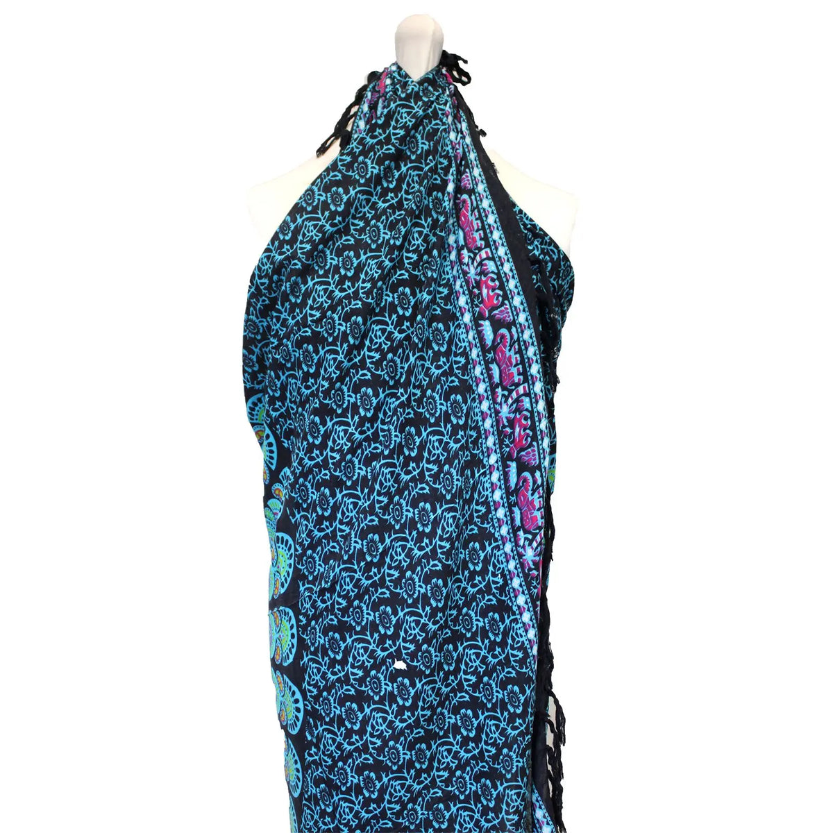 Pareo de tela negra con estampado floral y geométrico en azul, con flecos y diseño tipo mandala en un maniquí.