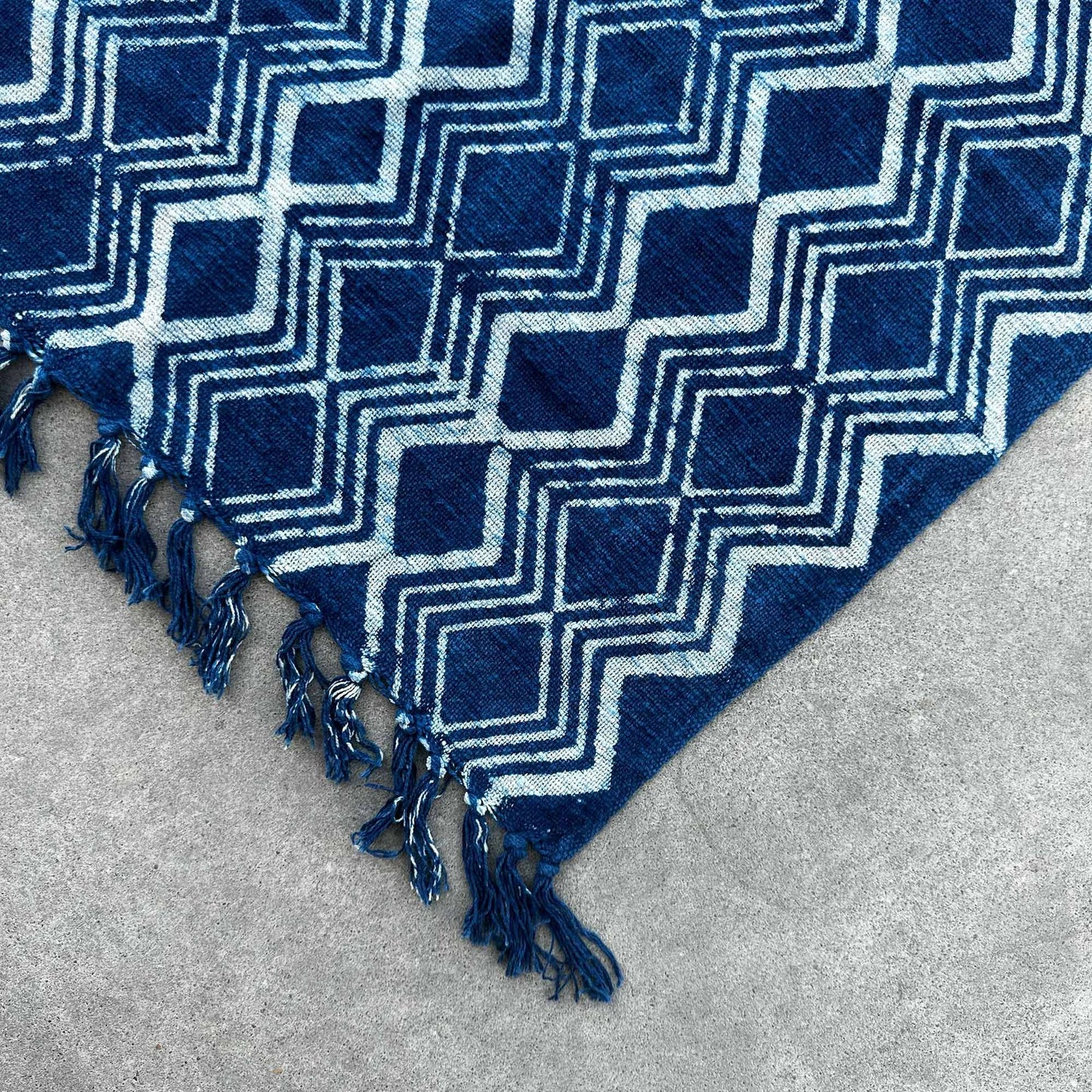 Alfombra azul con patrón geométrico en blanco, hecha de material suave, con flecos en los bordes.