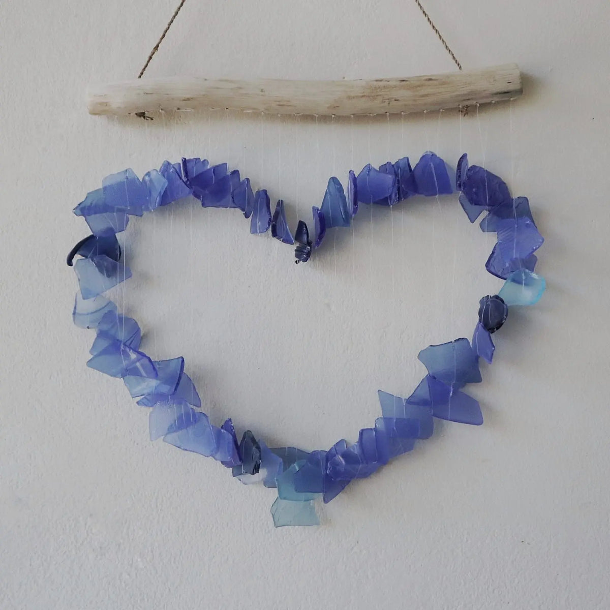 Carillón de pared con forma de corazón hecho con fragmentos de vidrio reciclado azul y blanco colgados de una rama.