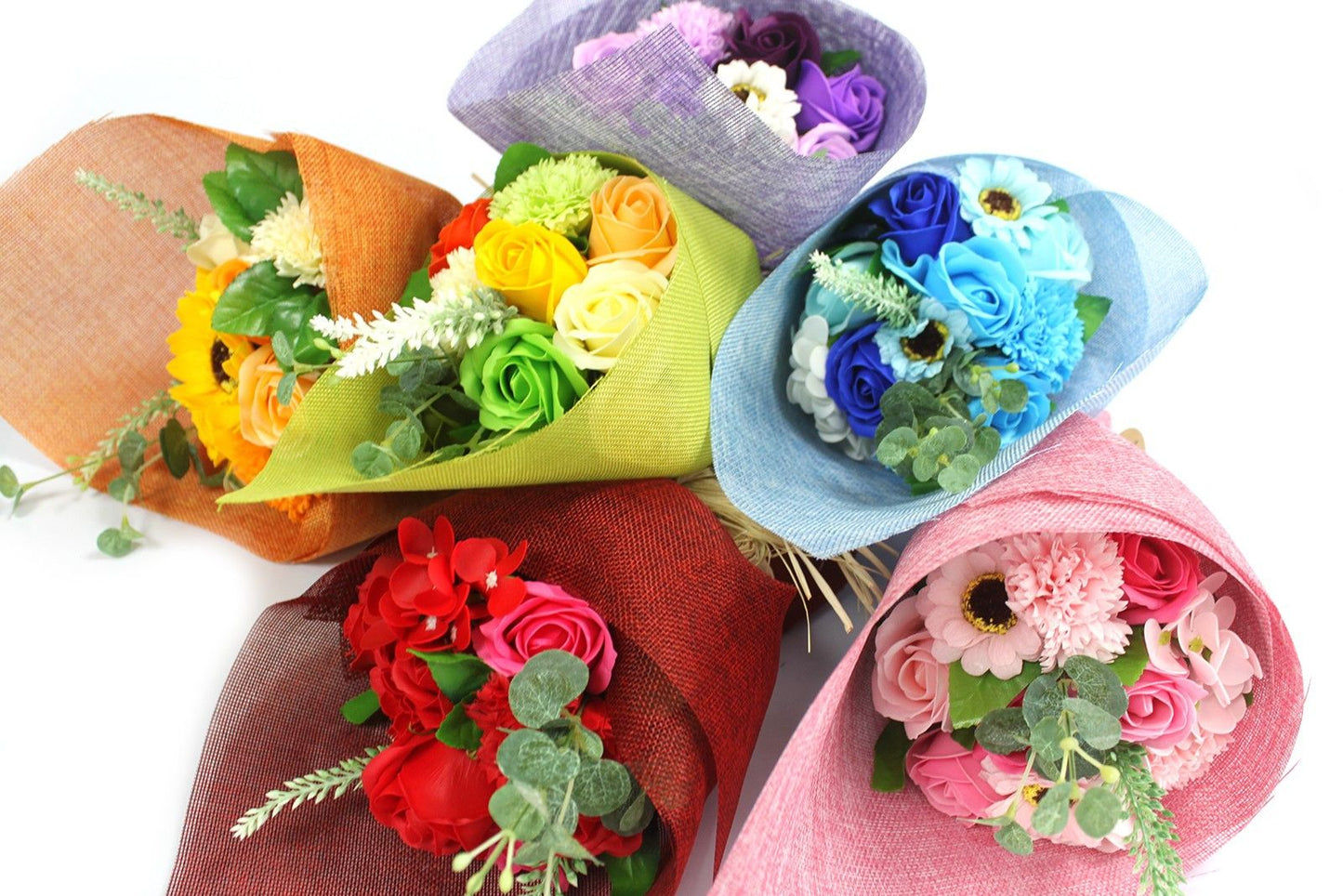 Cinco ramos de flores de jabón coloridos, envueltos en papel decorativo y con follaje verde sobre fondo blanco.