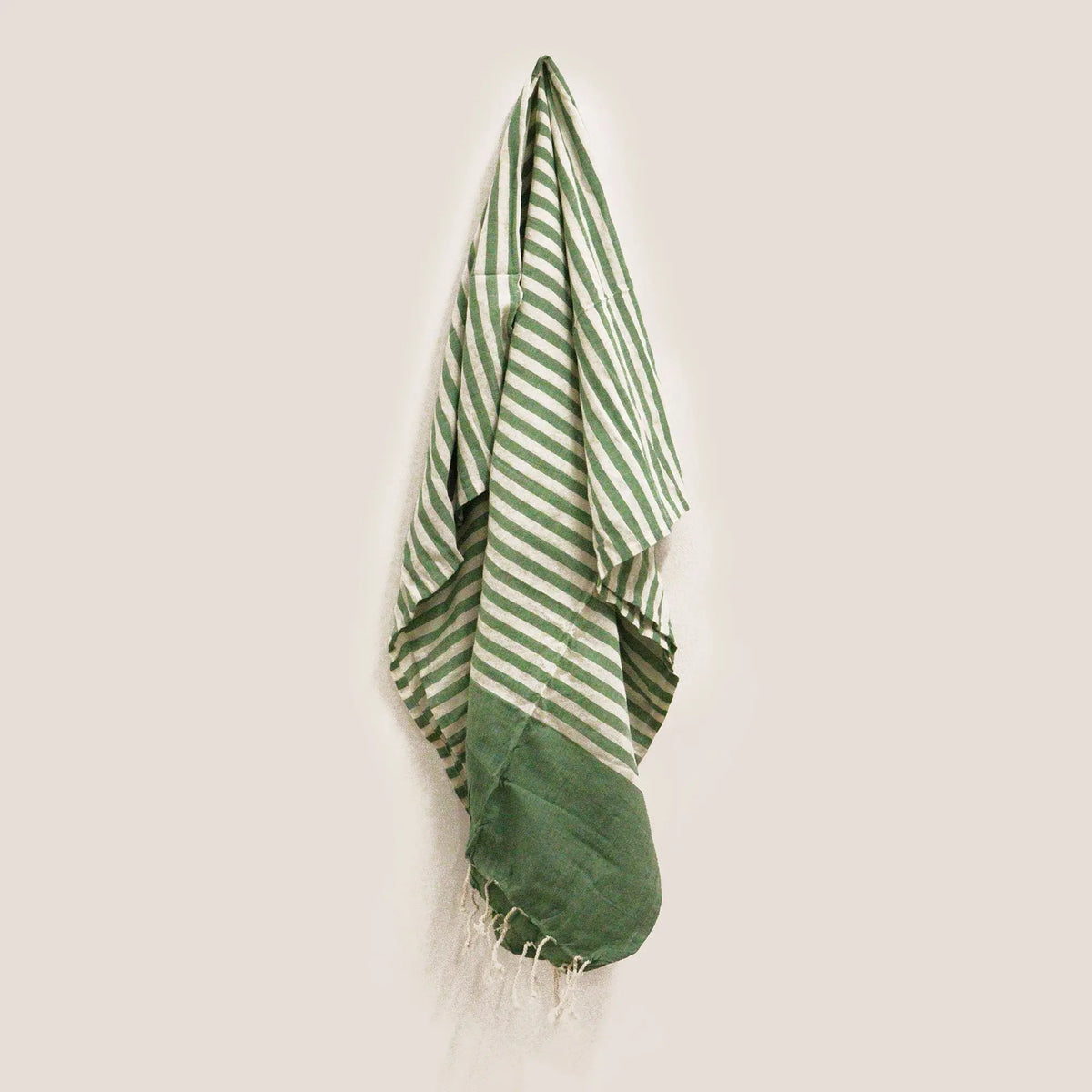 Manta pareo de algodón a rayas verdes y blancas con flecos, colgada verticalmente sobre un fondo liso.