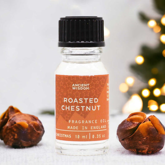 Frasco de 10 ml de aceite de fragancia con etiqueta naranja, entre dos castañas sobre fondo de luces navideñas.