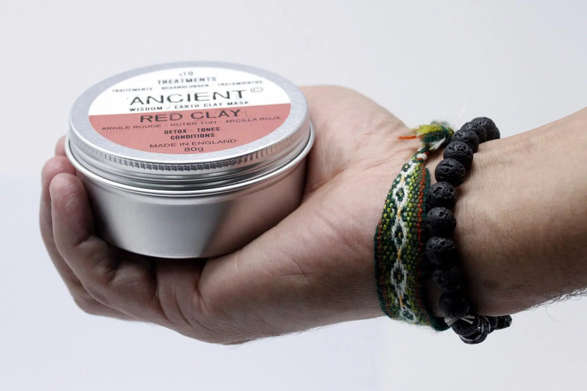 Mano sosteniendo una lata redonda de aluminio con etiqueta de mascarilla de arcilla roja de 80g.