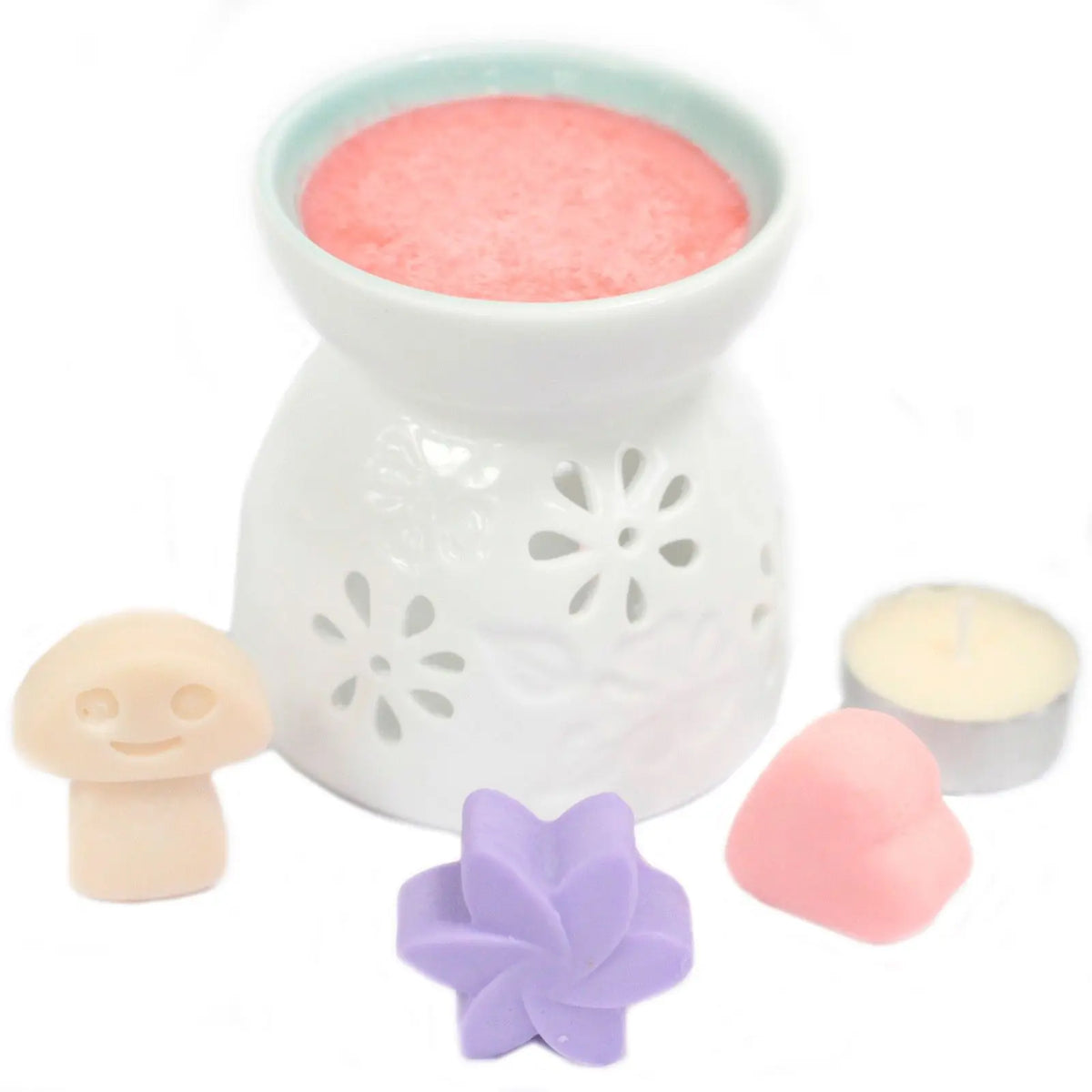 Quemador de cerámica blanco con cera rosa, acompañado de figuras de cera con formas de seta, flor y corazón.