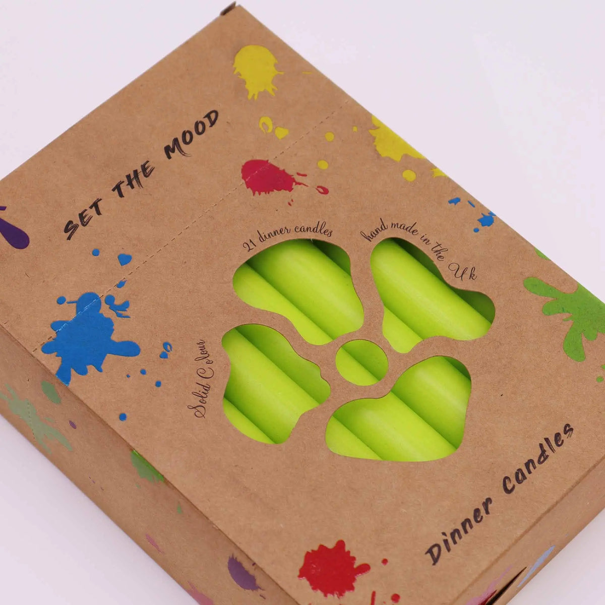 Caja de cartón kraft con manchas de colores que contiene 21 velas de mesa verde lima visibles a través de una abertura.