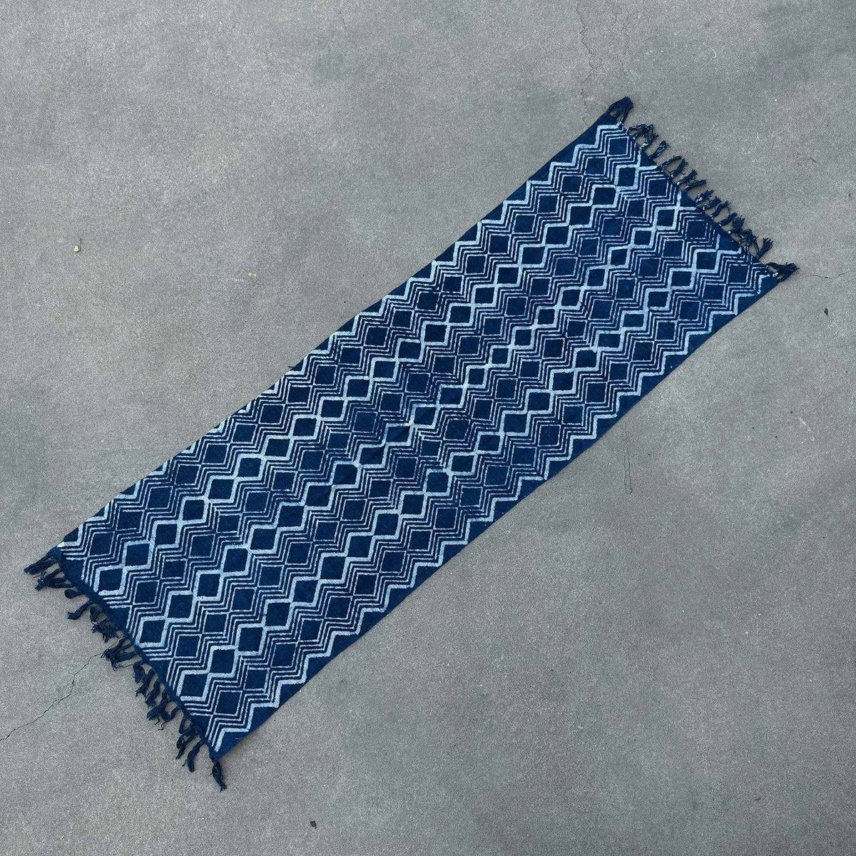 Alfombra azul marino con diseño geométrico y flecos, hecha de algodón, ideal para espacios modernos.