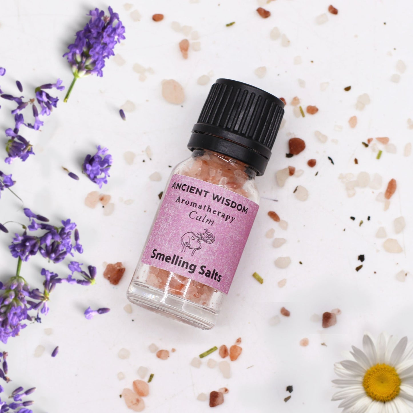 Frasco de vidrio con sales rosadas, etiqueta rosa y tapón negro, rodeado de flores de lavanda y sal esparcida.
