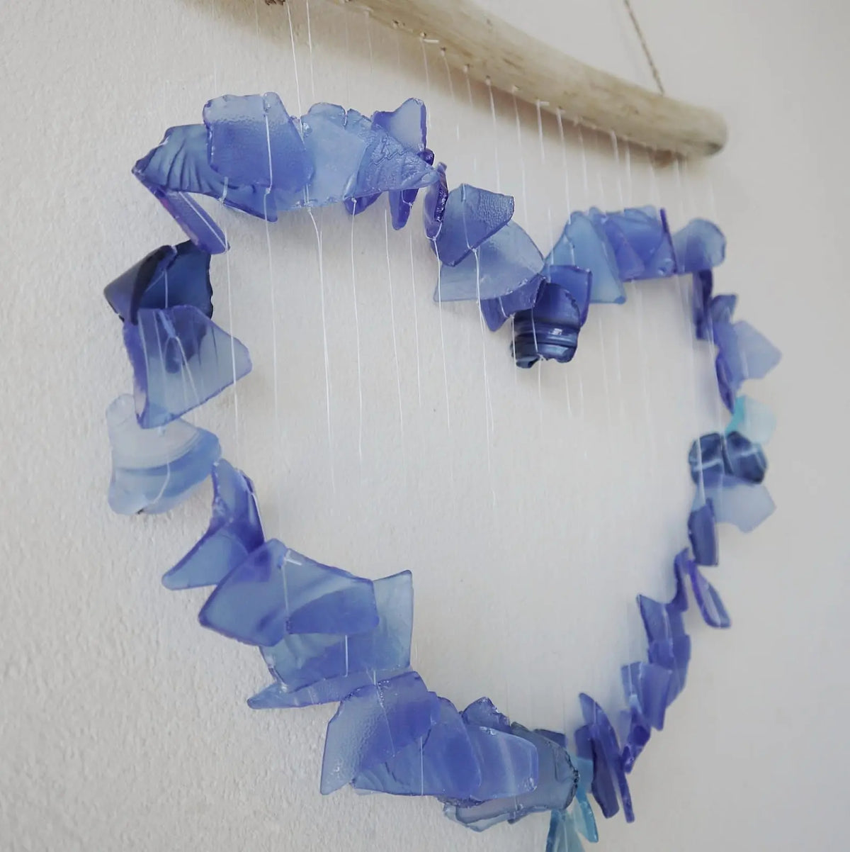 Carillón de vidrio reciclado azul y blanco, con forma de corazón, suspendido de una rama de madera natural.