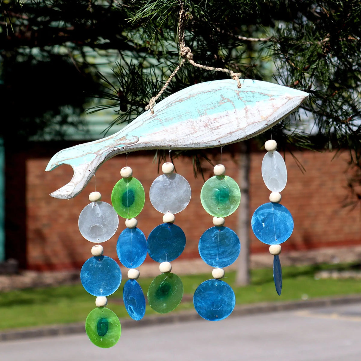 Carillón de madera con forma de pez rústico, colgantes de cuentas y discos translúcidos azules, verdes y blancos.