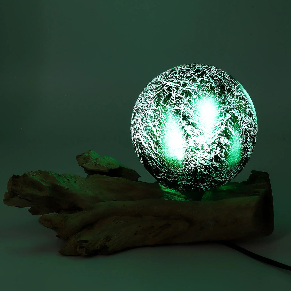 Lámpara esférica de cristal verde con acabado craquelado iluminada, sobre una base de madera natural.
