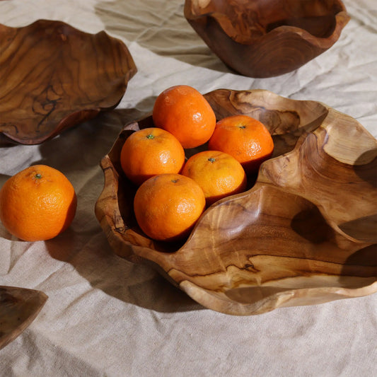 Frutero redondo de madera de teca con tres secciones, estilo orgánico, conteniendo mandarinas sobre tela beige.