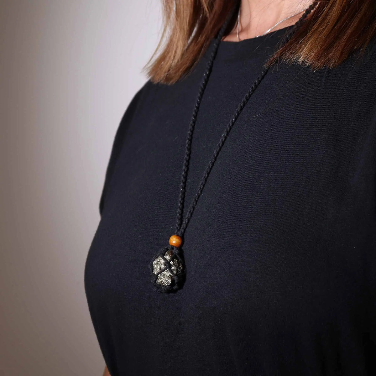 Collar de cordón negro trenzado con piedra preciosa bruta en red y cuenta de madera sobre camiseta negra.