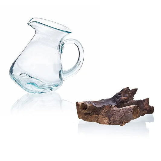 Jarra de vidrio soplado transparente junto a un trozo de madera natural rústica sobre fondo blanco