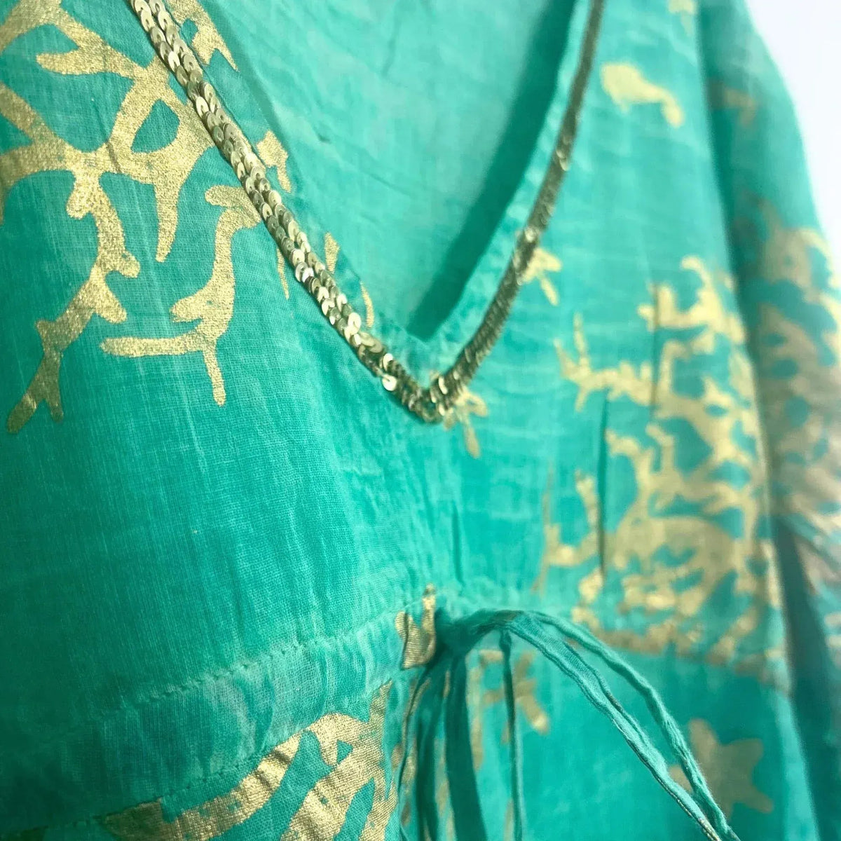 Vestido turquesa con estampado de corales dorados, cuello en V con detalle de lentejuelas y cordón ajustable.