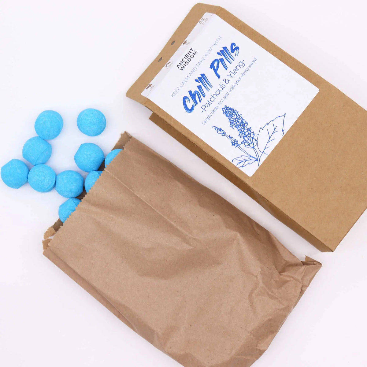 Mini bombas de baño esféricas azules saliendo de una bolsa de papel kraft con etiqueta informativa blanca.