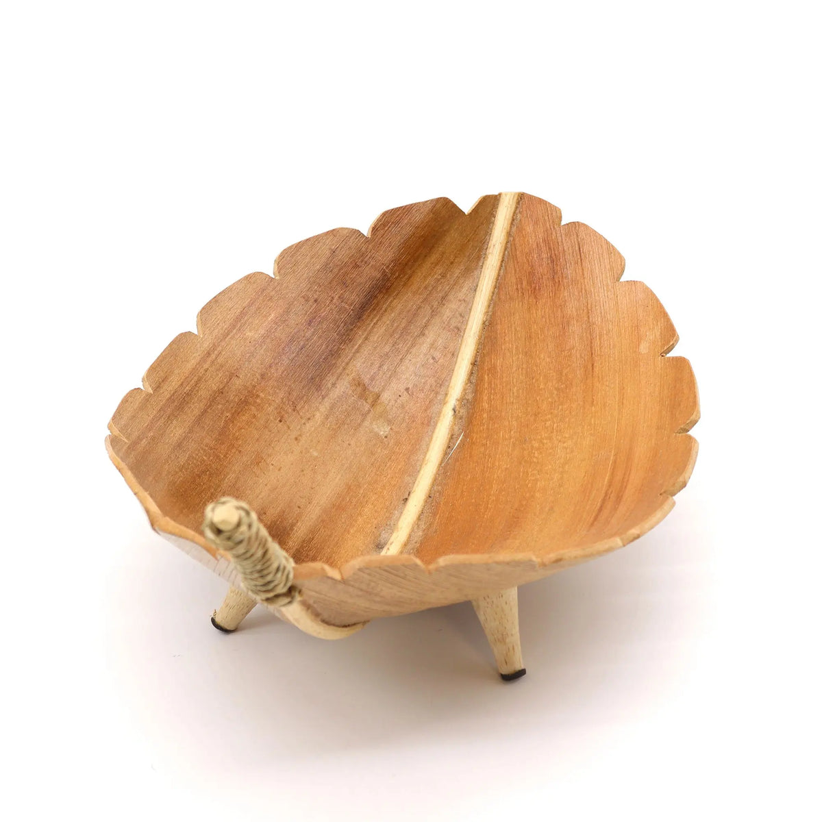 Frutero artesanal de hoja de coco natural con forma de hoja, sobre tres pequeñas patas de madera sobre fondo blanco.