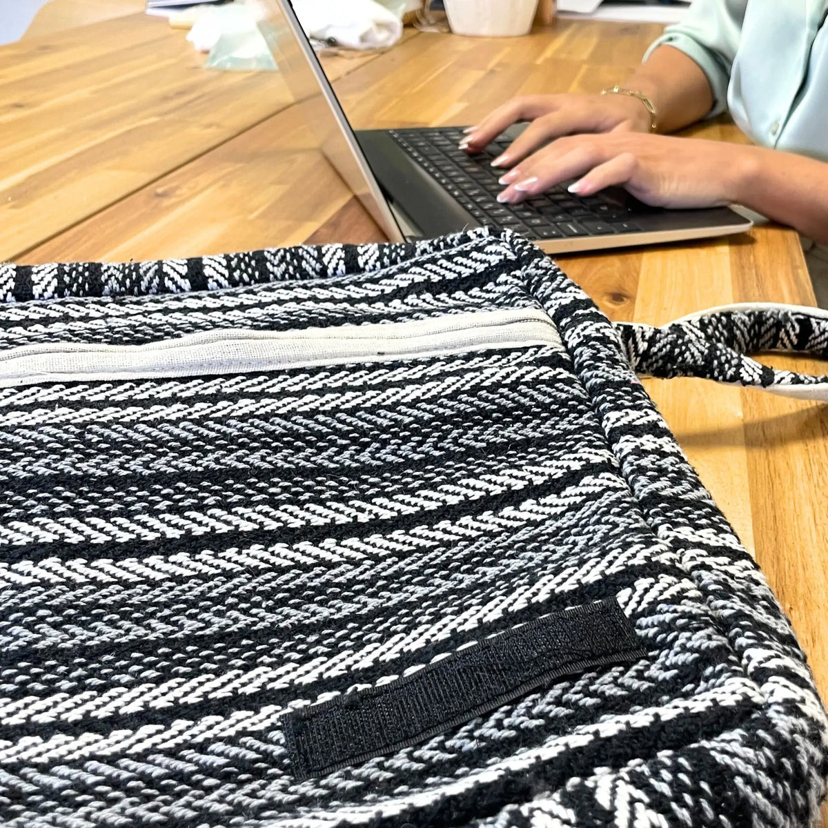 Bolso para portátil de tela con patrón de rayas tejidas en blanco y negro, cierre de cremallera y correa ajustable.