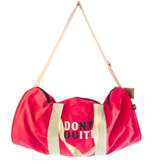 Bolsa de gimnasio rosa cereza con correas beige, diseño cilíndrico y texto negro "DONT QUIT!" en la parte central.
