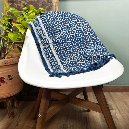 Manta azul con diseño floral en algodón, decorando una silla blanca moderna. Perfecta para decorar y abrigar.