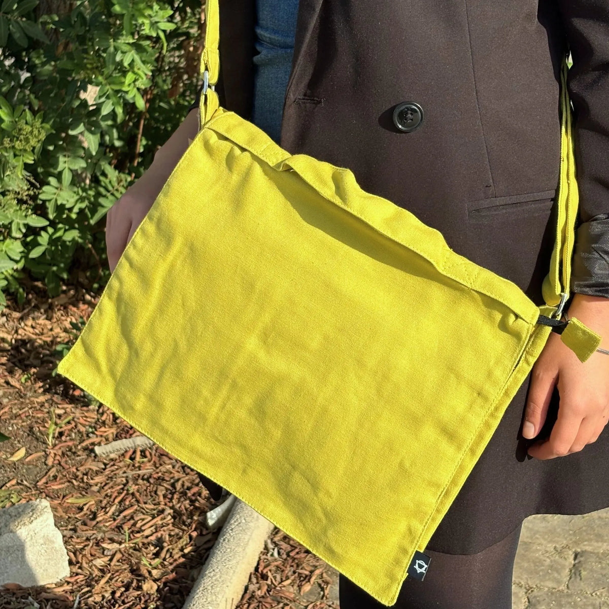 Bolsa mensajera de lona color mostaza, diseño rectangular minimalista con correa ajustable, estilo casual y funcional.