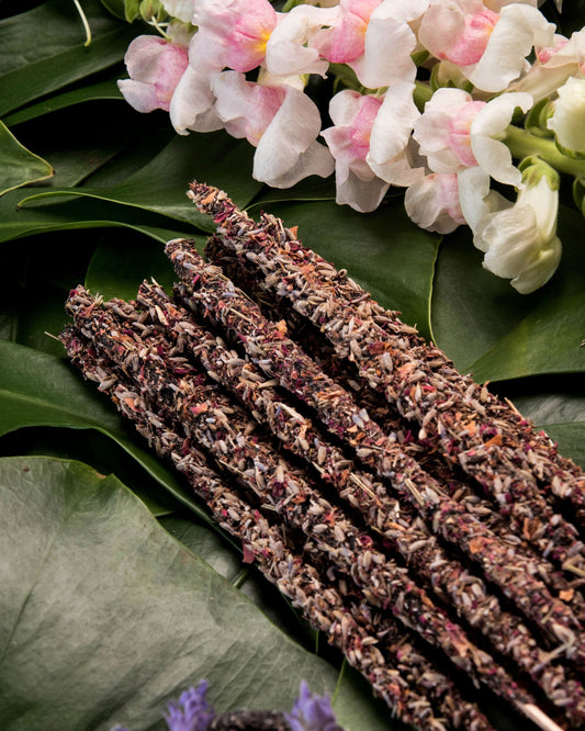Varitas de incienso botánico con lavanda y pétalos, sobre hojas verdes y flores blancas, estilo natural y artesanal