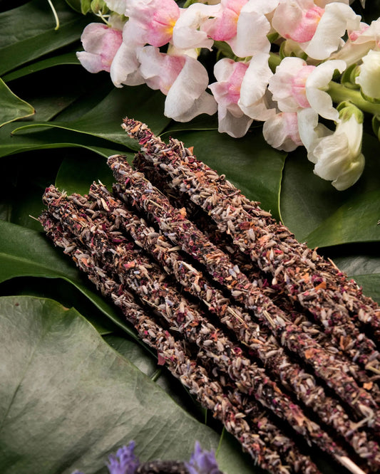 Varitas de incienso botánico con lavanda y pétalos, sobre hojas verdes y flores blancas, estilo natural y artesanal