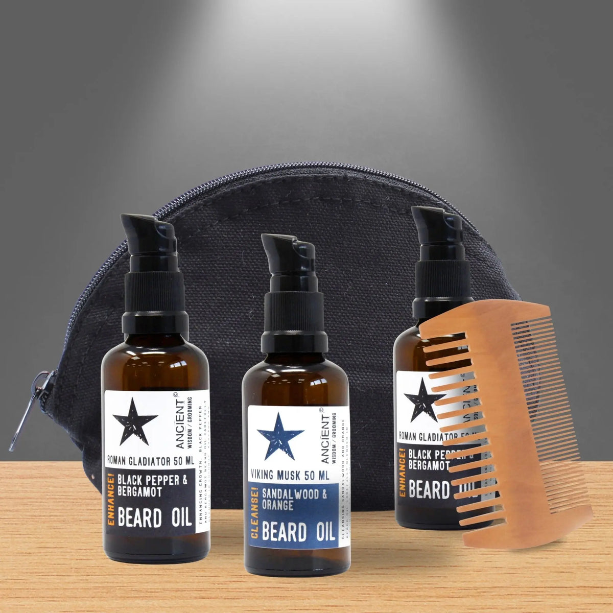 Set de regalo Ancient Wisdom: 3 aceites para barba en frascos ámbar, peine de madera y neceser negro sobre base de madera.