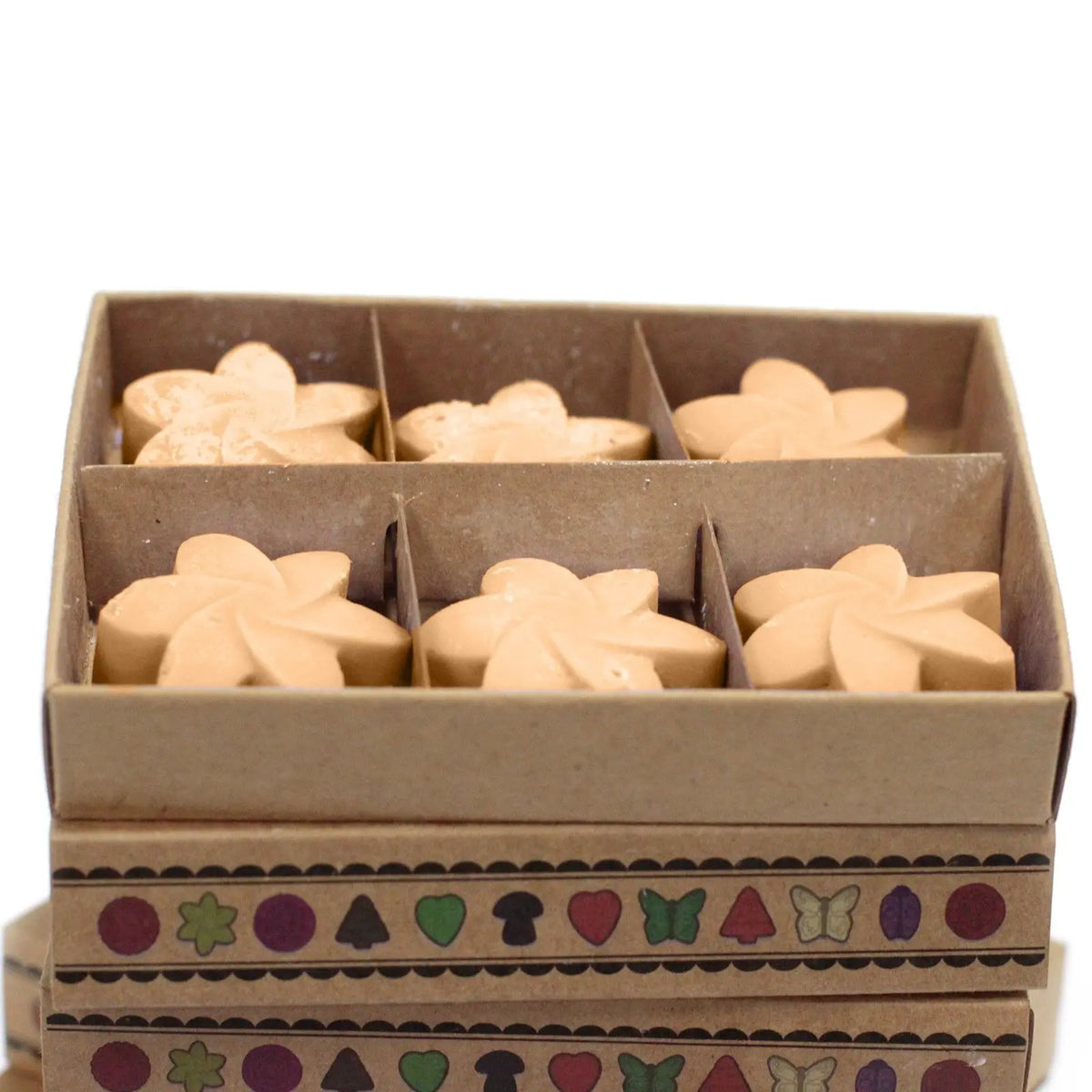 Caja de cartón con 6 ceras de soja beige en forma de flor, decorada con motivos geométricos y figuras de colores.
