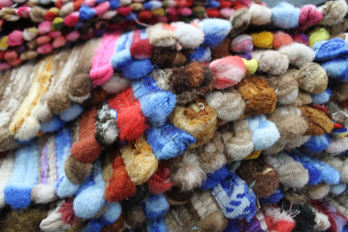 Alfombra artesanal de trapo tejida en tonos multicolor con textura suave, estilo rústico y acabado detallado.