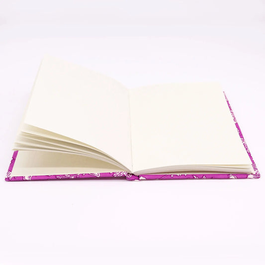 Cuaderno abierto con tapa de algodón fucsia estampado, páginas blancas, formato rectangular sobre fondo blanco.