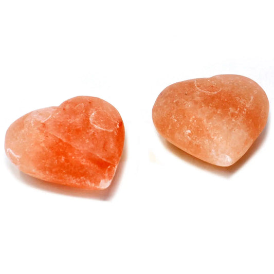 Dos piedras de sal mineral del Himalaya con forma de corazón, color rosa anaranjado, sobre fondo blanco.