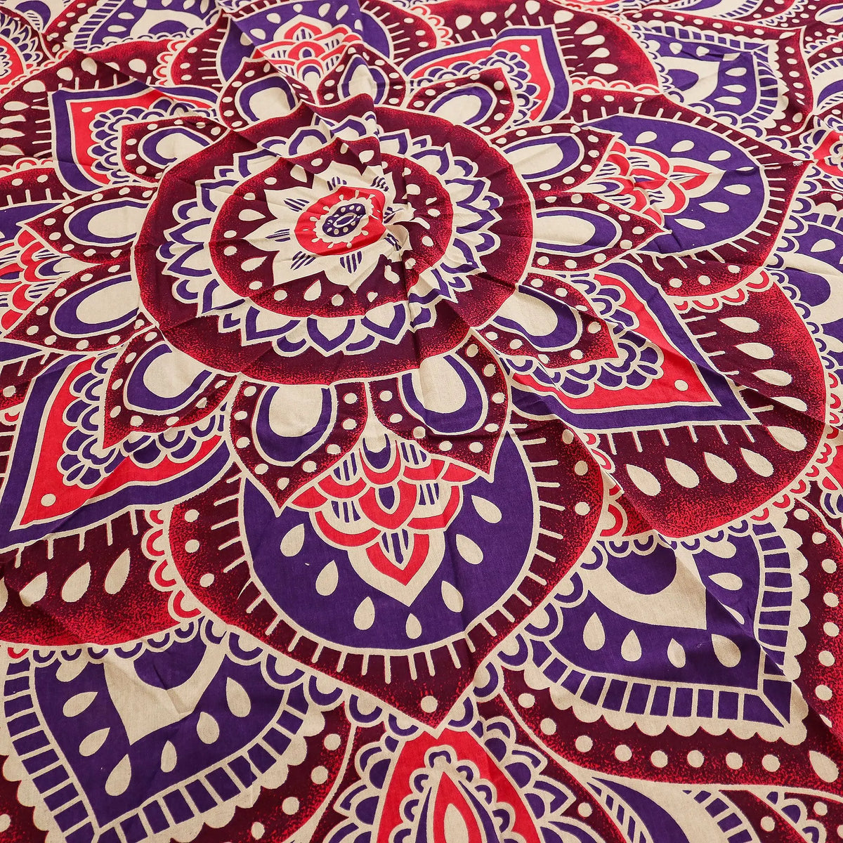 Tapiz redondo de algodón con diseño de mandala en tonos rosa y morado sobre fondo crema, estilo decorativo bohemio.