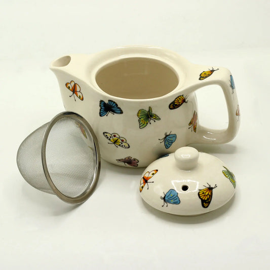 Tetera de cerámica color crema con estampado de mariposas, incluye tapa y filtro metálico para hierbas.