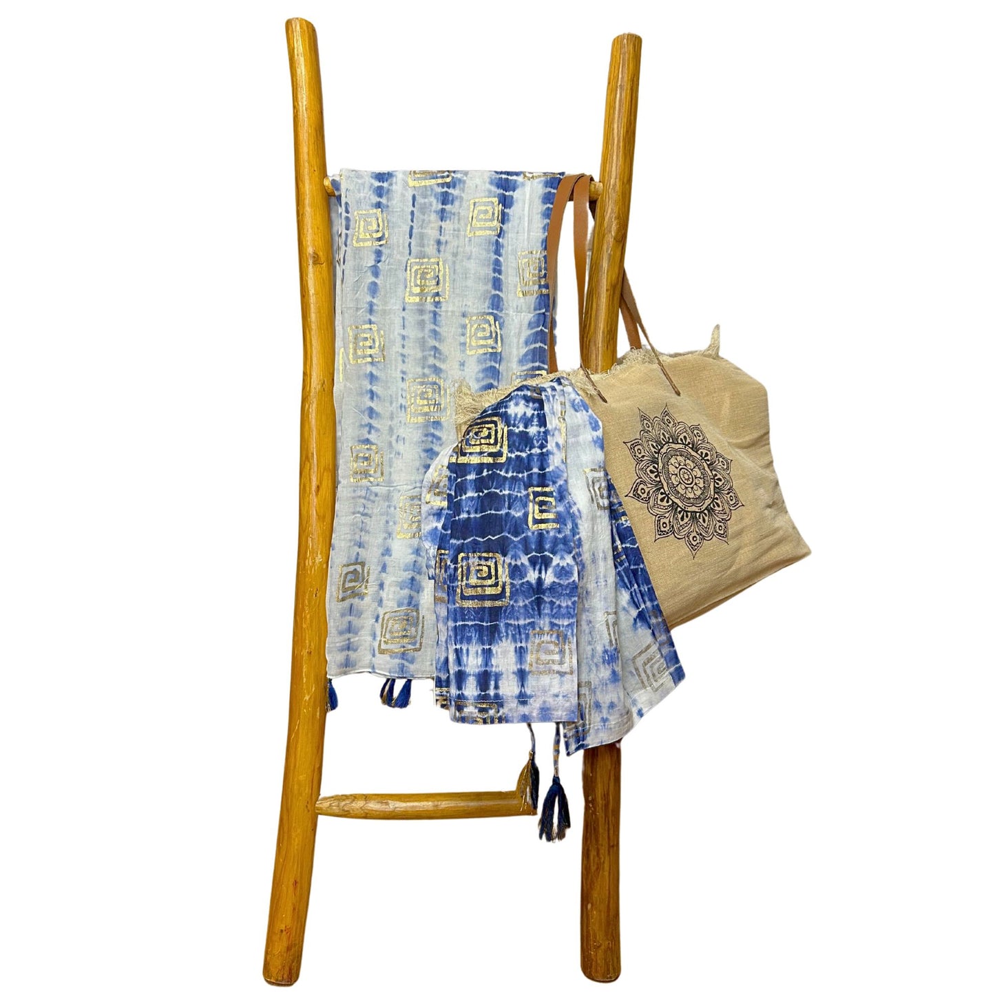 Pareo azul tie-dye con estampado dorado en escalera de madera, junto a un bolso de yute con diseño de mandala.