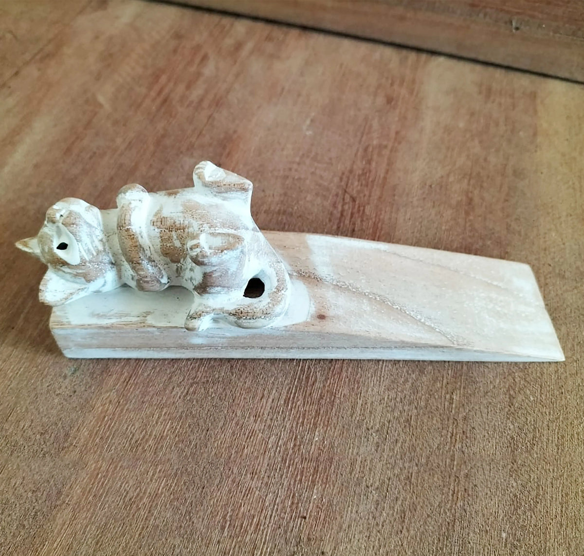 Tope de puerta de madera tallada con forma de gatito acostado, acabado en tonos madera natural y pintura blanca.