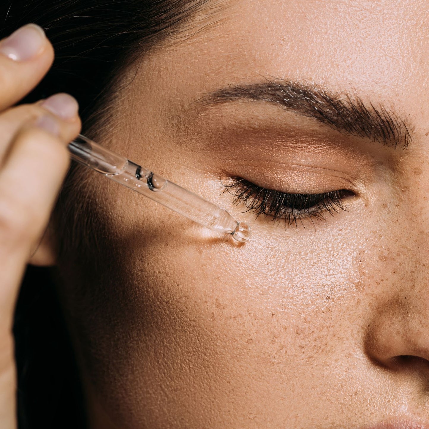 Primer plano de mujer aplicando serum facial de Vitamina C Ancient Wisdom con un gotero de cristal sobre su piel.
