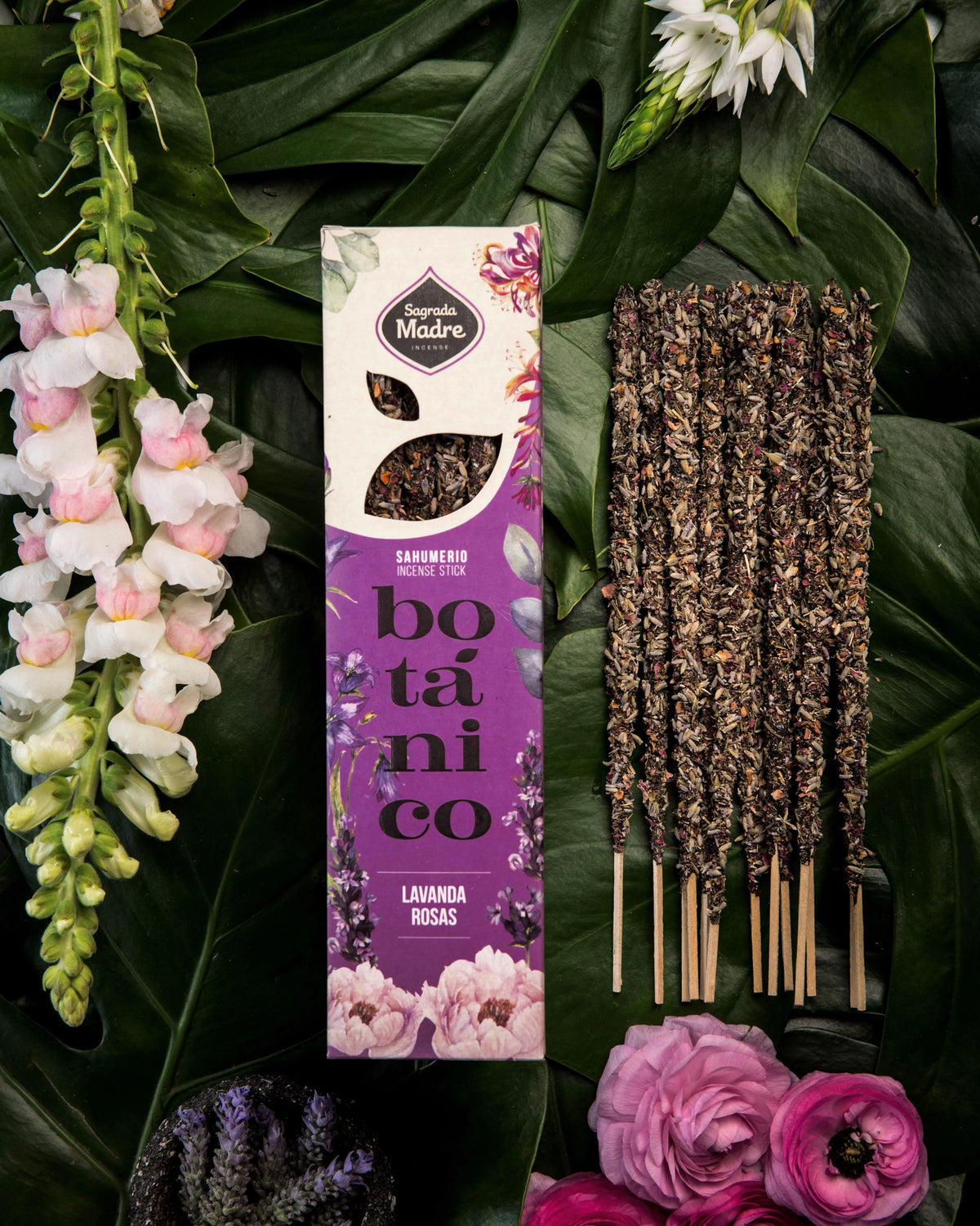 Caja de sahumerios de lavanda y rosas junto a varillas artesanales sobre hojas verdes, flores y una base de madera.