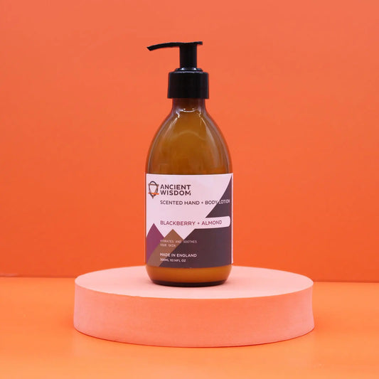 Loción corporal de mora y almendra en envase de vidrio ámbar con dosificador negro, sobre base rosa. Fondo naranja.