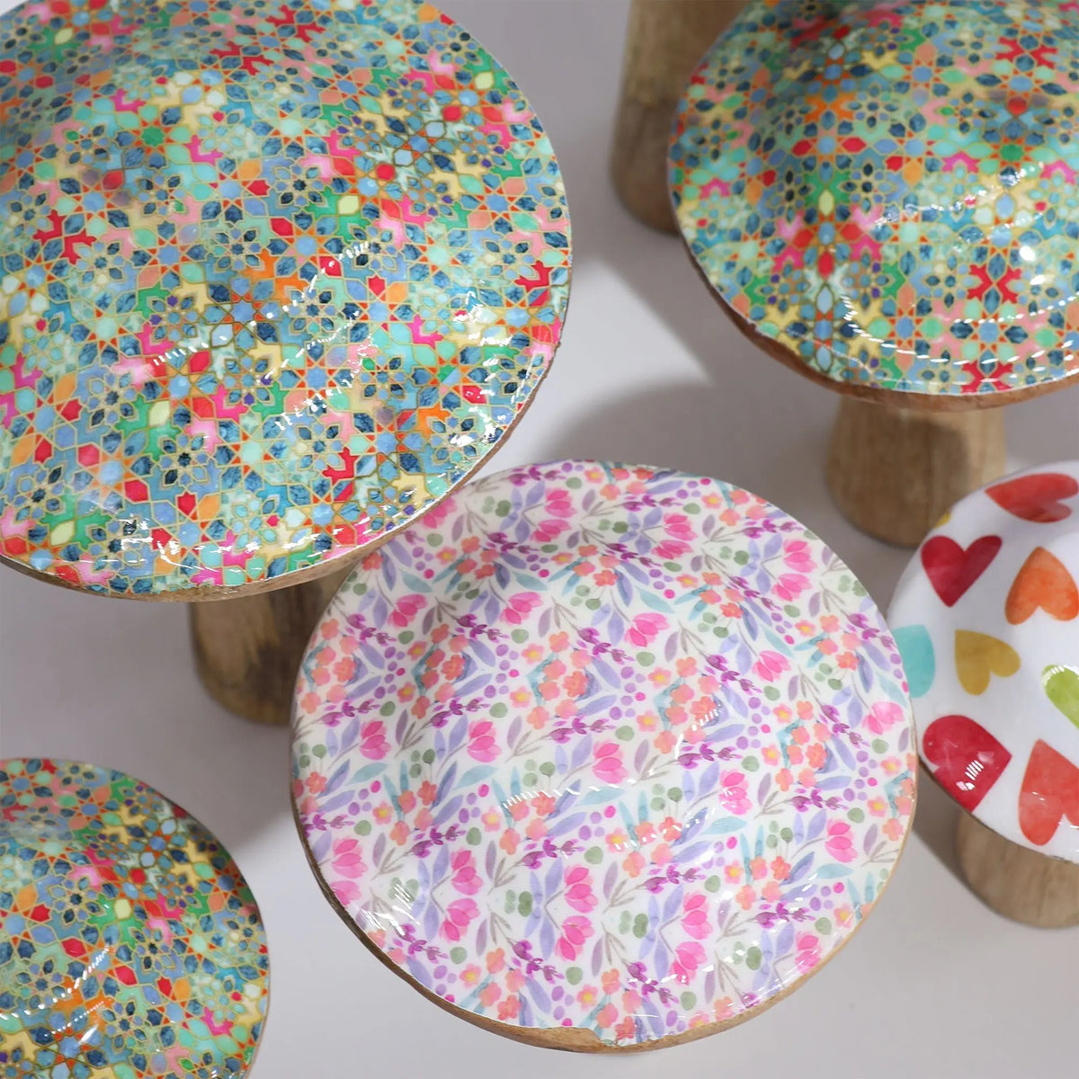 Setas decorativas de madera esmaltada con variados estampados coloridos, geométricos y florales, sobre fondo blanco.