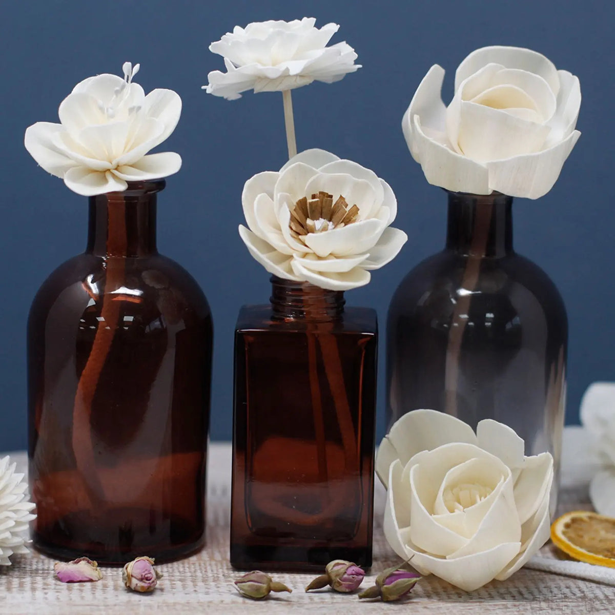 Flores difusoras de madera de sola en frascos de cristal oscuro con cordón absorbente y decoración natural.