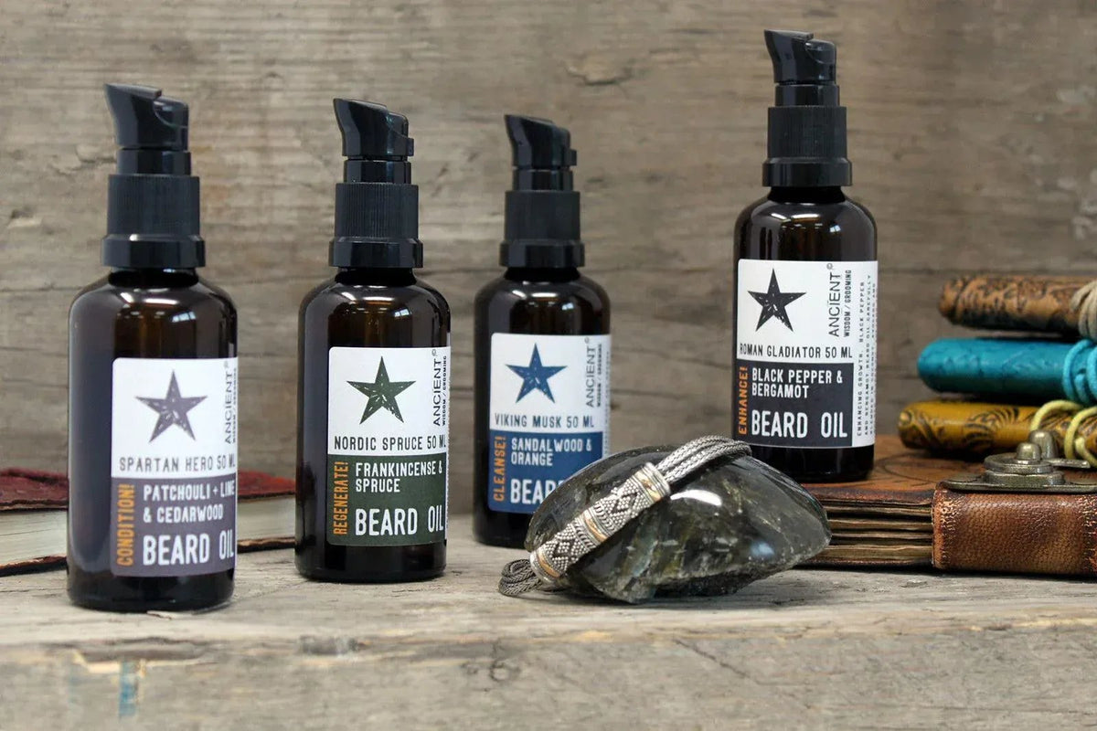 Cuatro frascos de aceite para barba Ancient Wisdom (50ml) con dosificador negro sobre fondo de madera rústica.