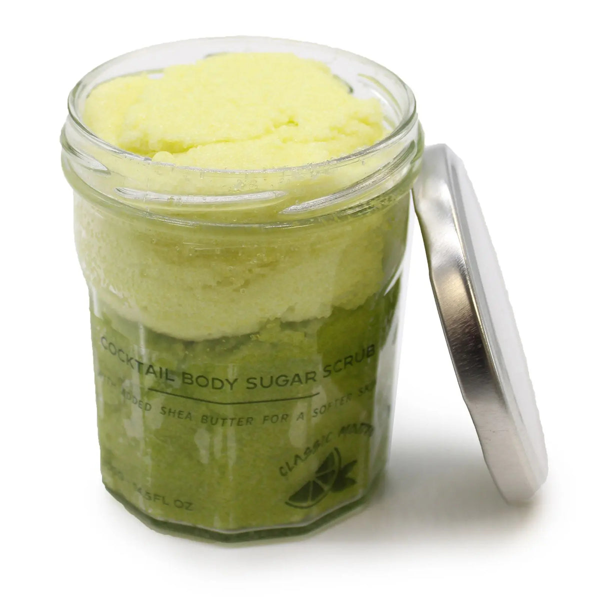 Tarro de cristal abierto con exfoliante de azúcar verde y amarillo sobre fondo blanco. Tapa metálica al lado.