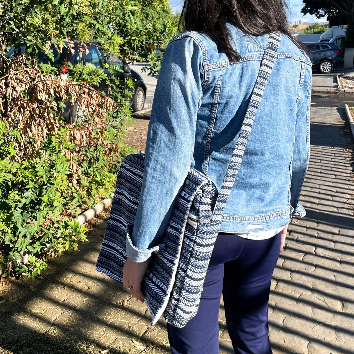 Bolso para portátil de tela con patrón de rayas azules y blancas, diseño tipo bandolera, sostenido bajo el brazo.