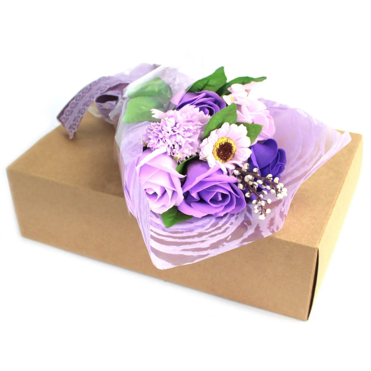 Bouquet de flores de jabón en tonos púrpura envuelto en papel decorativo sobre una caja de regalo de cartón.