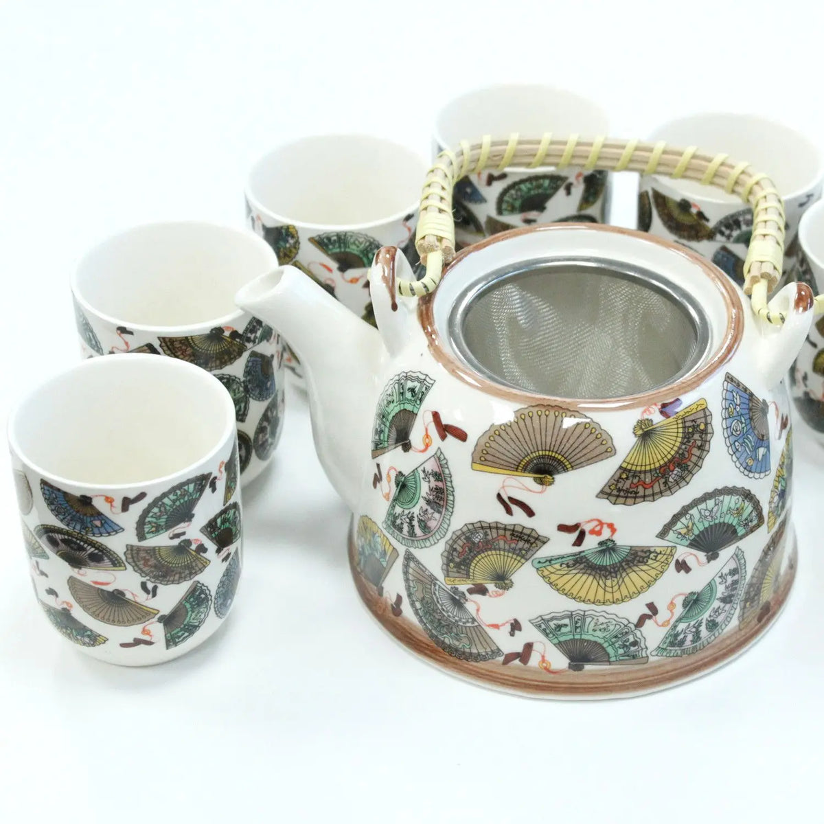 Tetera de cerámica blanca con diseño de abanicos, colador metálico, asa de mimbre y seis tazas a juego.