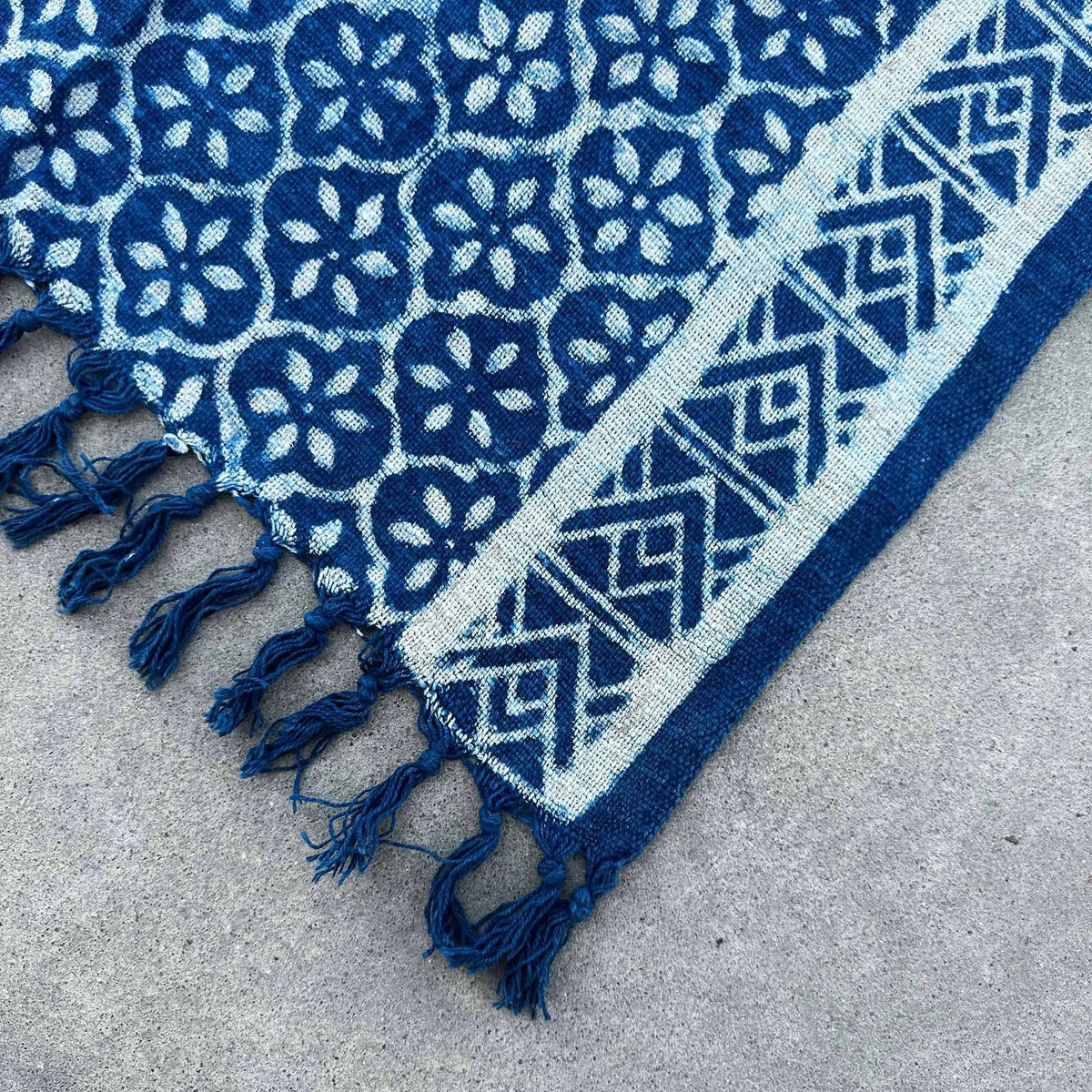 Manta azul con diseño floral y geométrico, fabricada en algodón, con flecos decorativos.