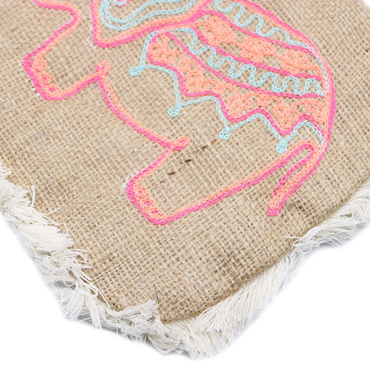 Bolso de yute color natural con flecos blancos y bordado de elefante en hilos de colores rosa y turquesa.