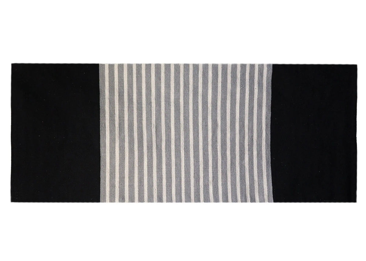 Alfombra rectangular de algodón, diseño a rayas gris y blanco en el centro y bordes laterales negros sólidos.